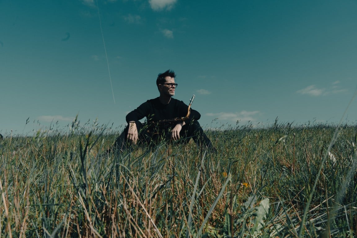 Donny McCaslin mit Saxophon auf einer Wiese, Promofoto